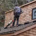 Cleaning rain gutter on roof with a power cleaner.