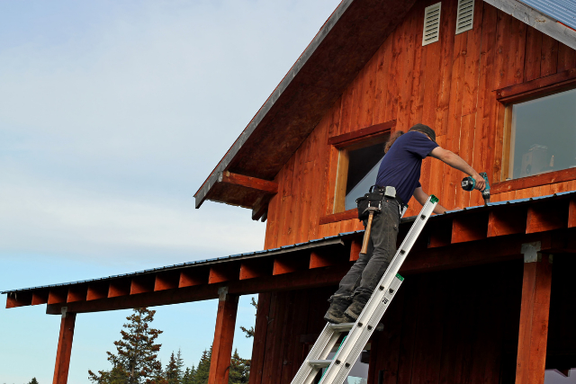 New Haven roof repairs by roofer on a ladder with power tool.