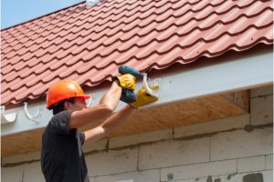 New gutter system being installed by worker with orange hard hat on and power tool.