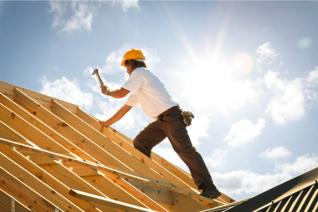 Re-roofing worker with a yellow hard hat on with a hammer.